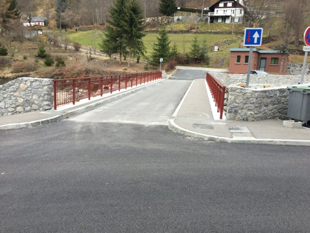 Pont routier rénové en montagne : balustrade rouge. Petit pont routier avec balustrade rouge, murs en pierre, et asphalte neuf en zone montagneuse. Panneau de priorité de passage.